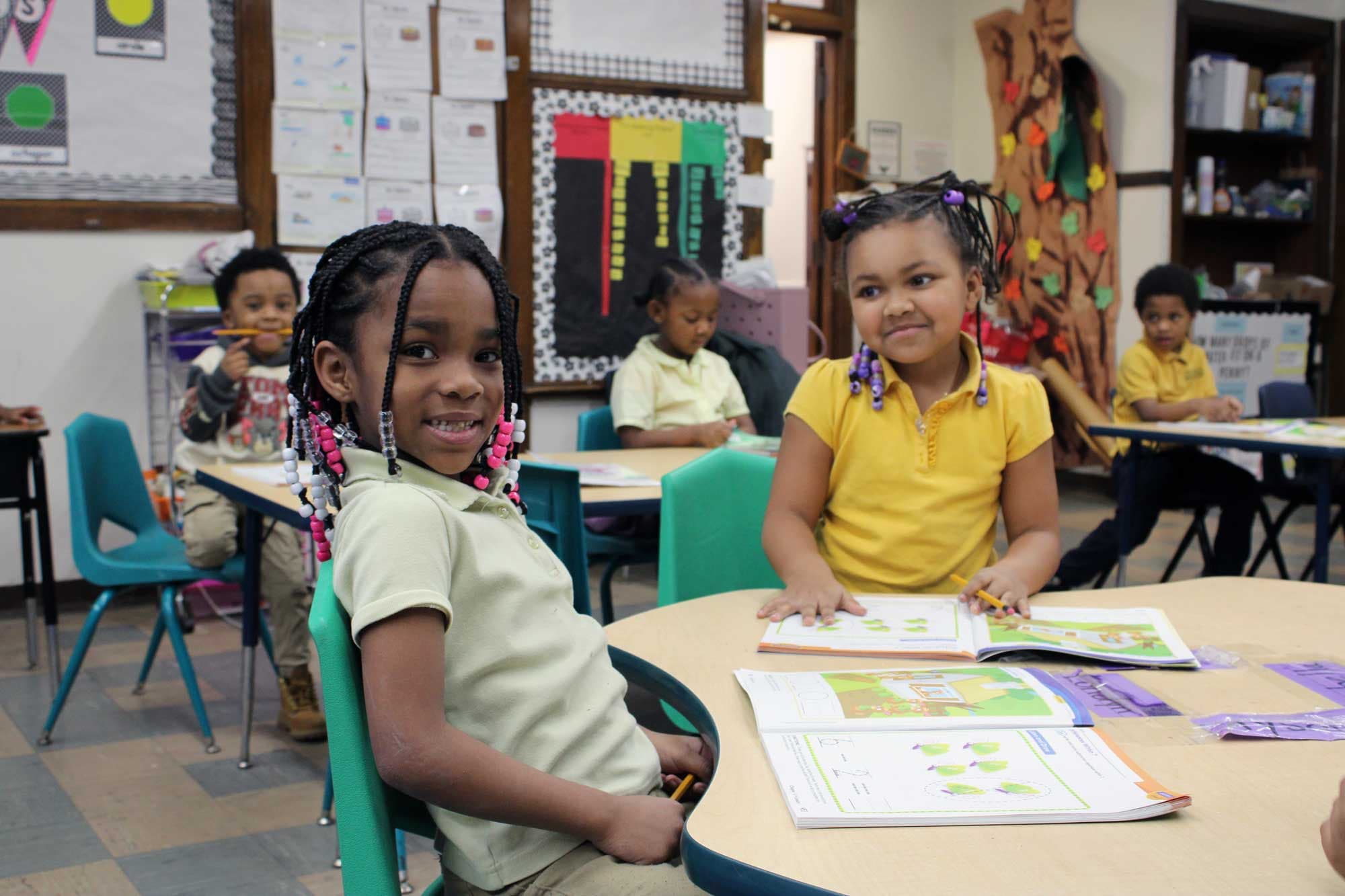 Young students working in workbooks at a classroom table.