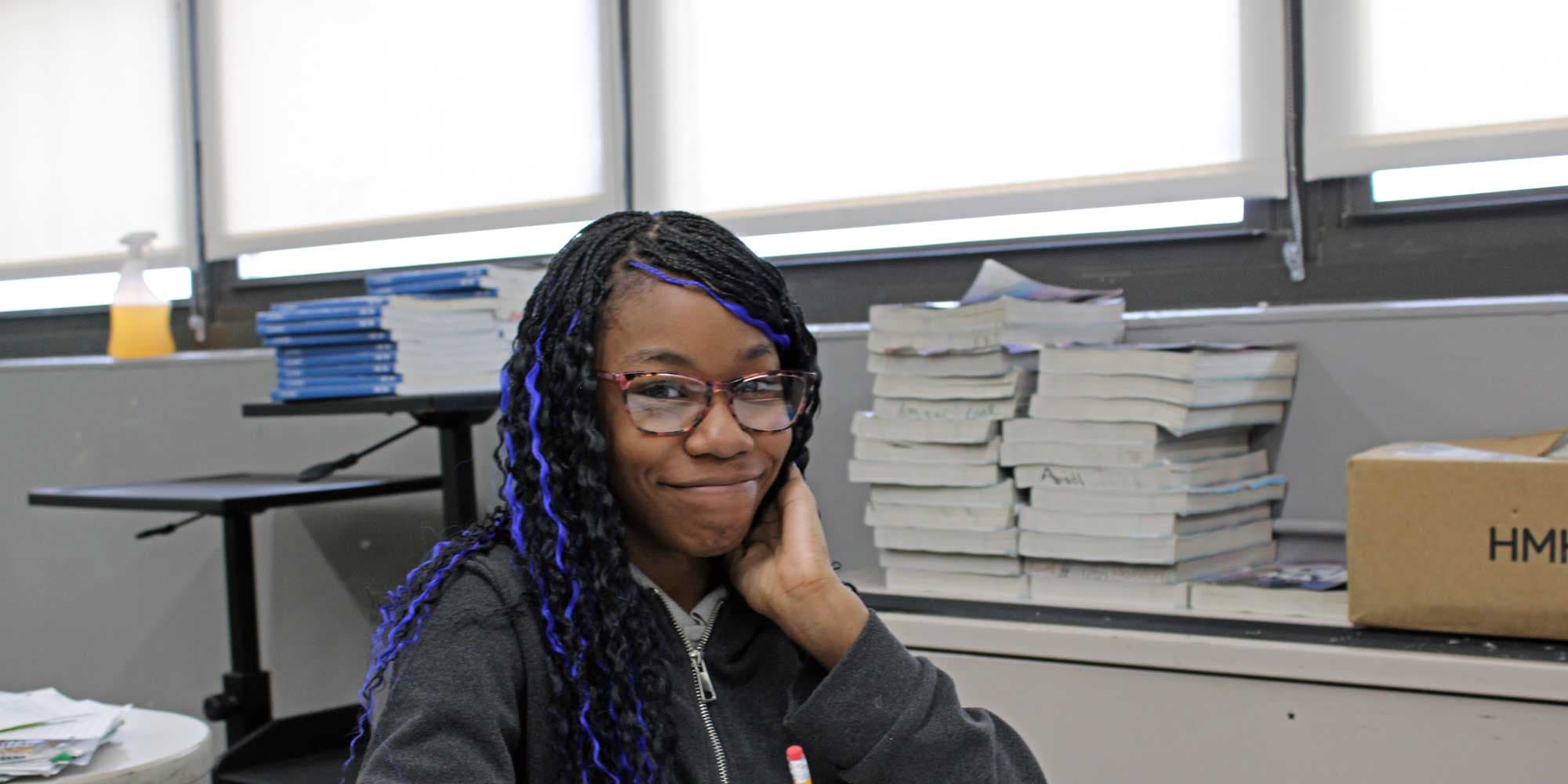 Smiling middle school student with glasses seated in a classroom.
