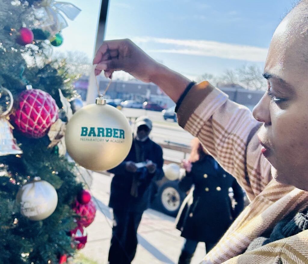 Adult hanging a gold ornament on a Christmas tree.