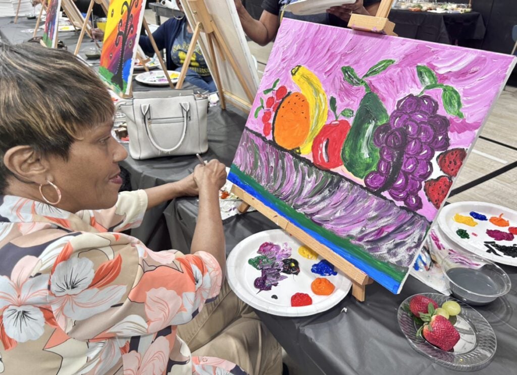 Adult painting a colorful still life of fruit on a canvas.