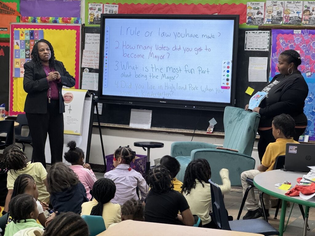 Adults and children in a classroom with an interactive display.