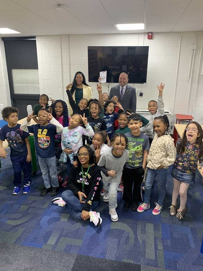 Two adults and many children smiling and posing in a classroom.