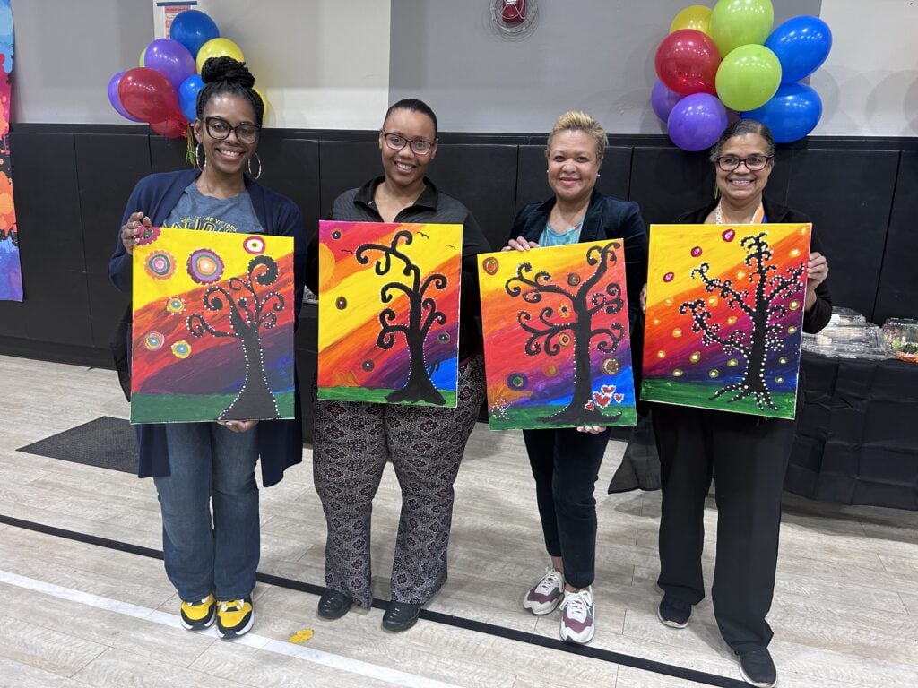 Four adults proudly display their colorful tree paintings.