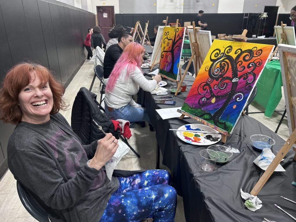 Adults painting colorful tree canvases at an event.