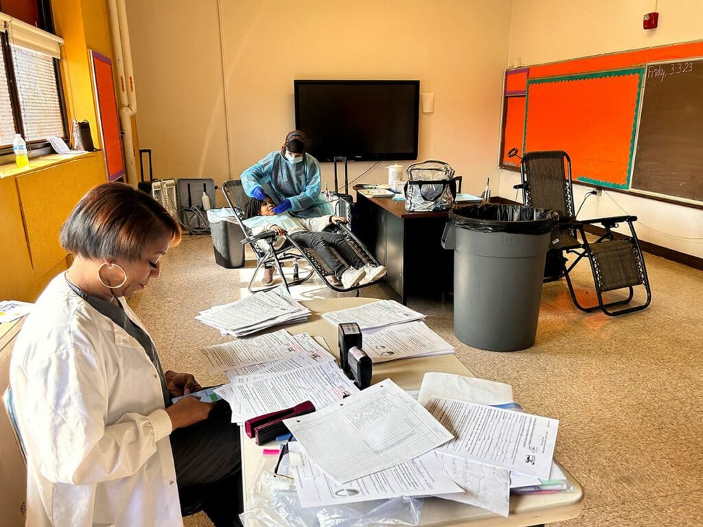 Two adults working in a classroom, one with papers, one with a child.