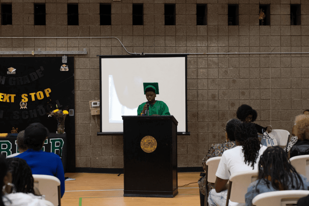 Child in green graduation attire speaking at a podium.