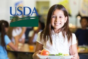Smiling child holding a lunch tray with an apple and salad, USDA logo.