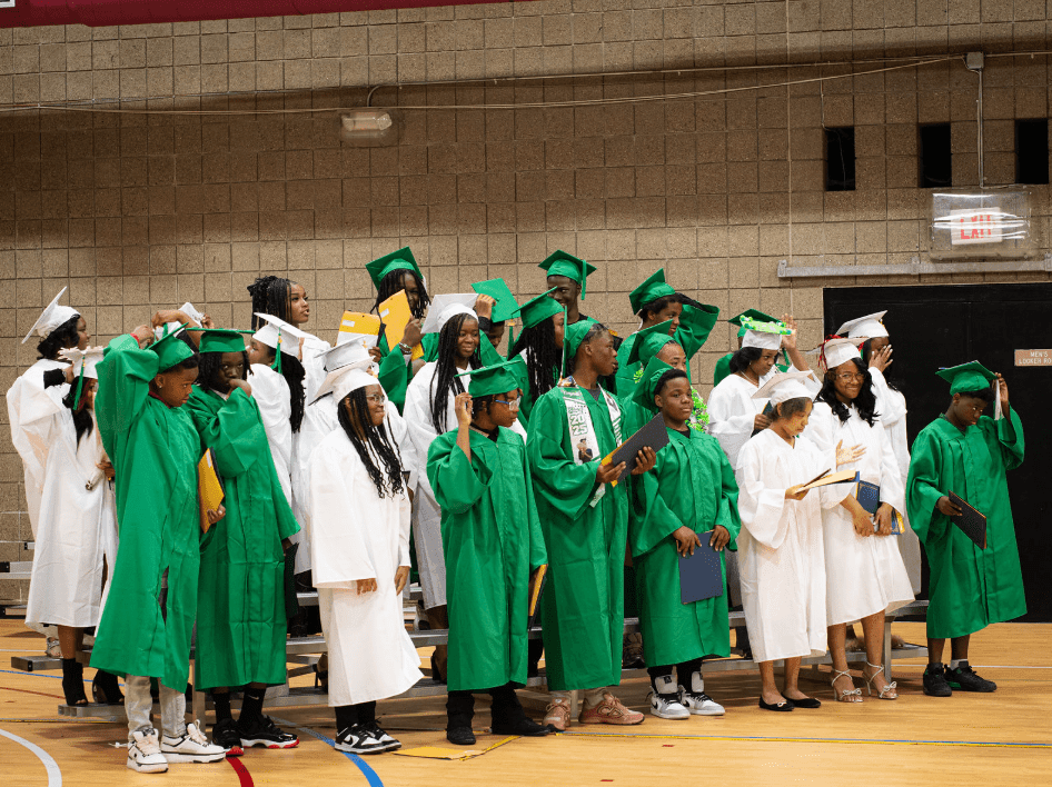 Children in green and white graduation gowns and caps.