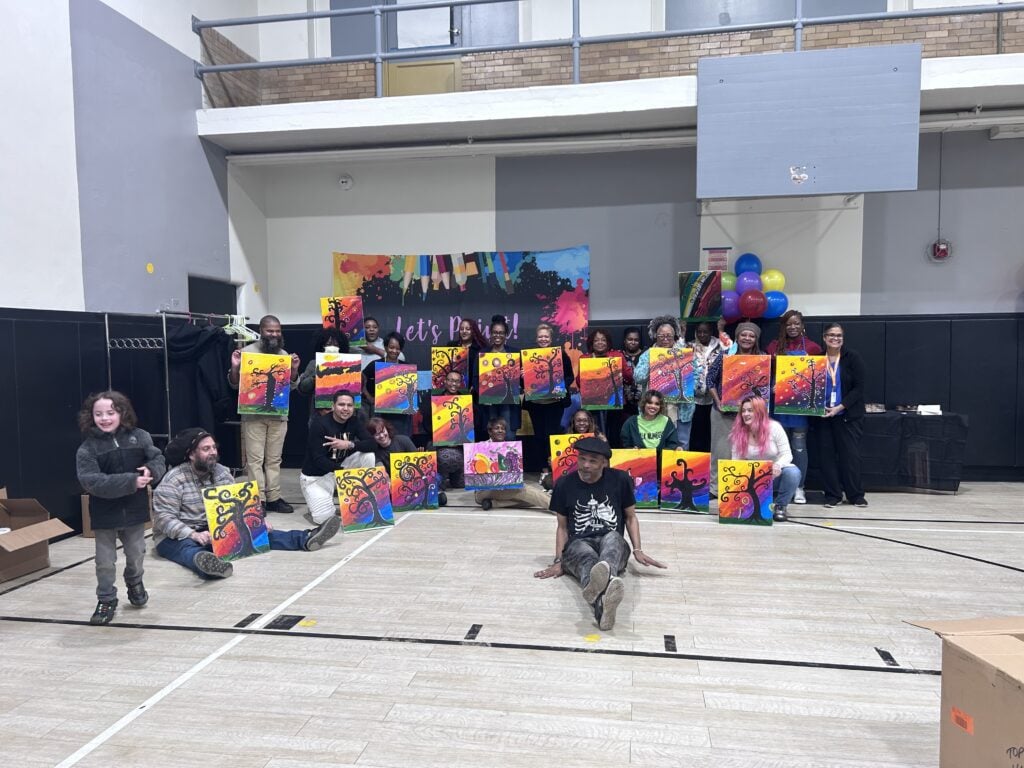 Adults and children proudly display their vibrant paintings in a gym.
