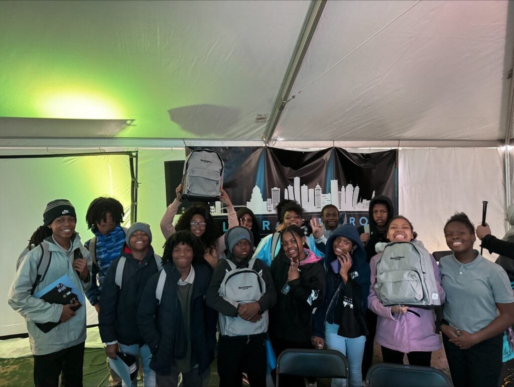 Children smiling and holding up gray backpacks.