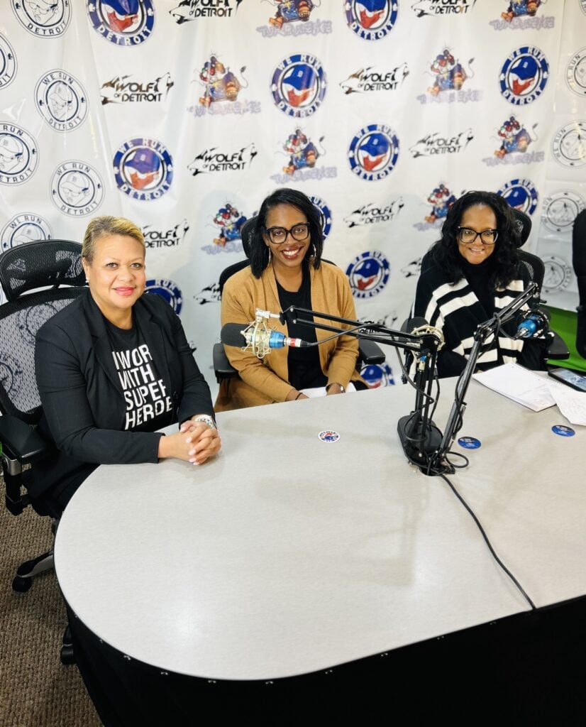 Three adults at a table with microphones, facing forward.